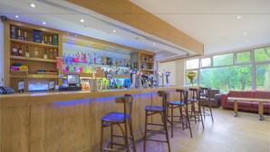 A bar area with wooden shelves stocked with bottles, a counter with a phone, and bar stools. - Cobden Hotel Birmingham (Birmingham)