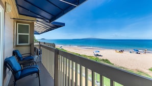 A balcony with a view of a beach, outdoor furniture, and a clear sky.