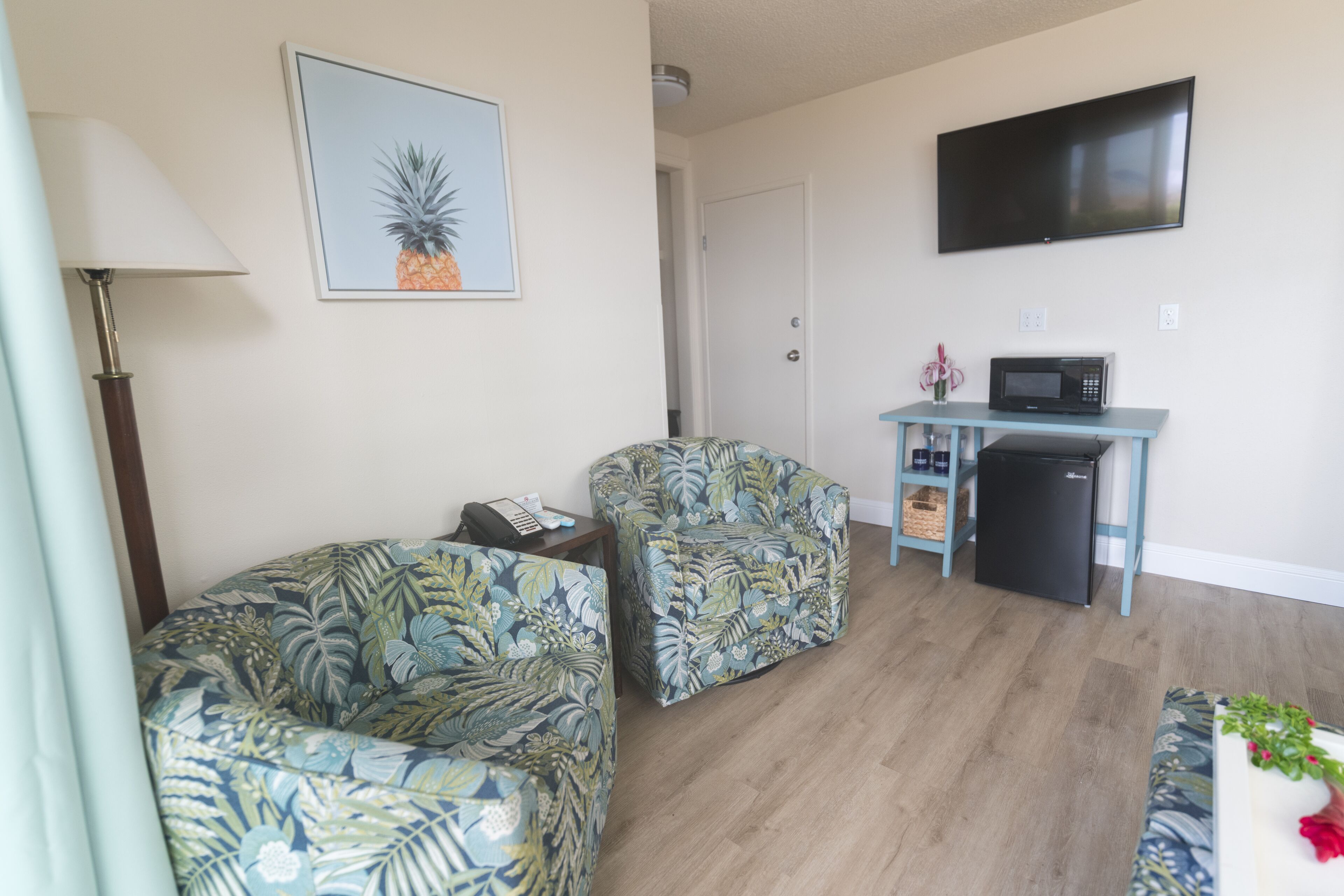 Sala de estar com dois sofás estampados, uma televisão de tela plana, um micro-ondas e um refrigerador pequeno.