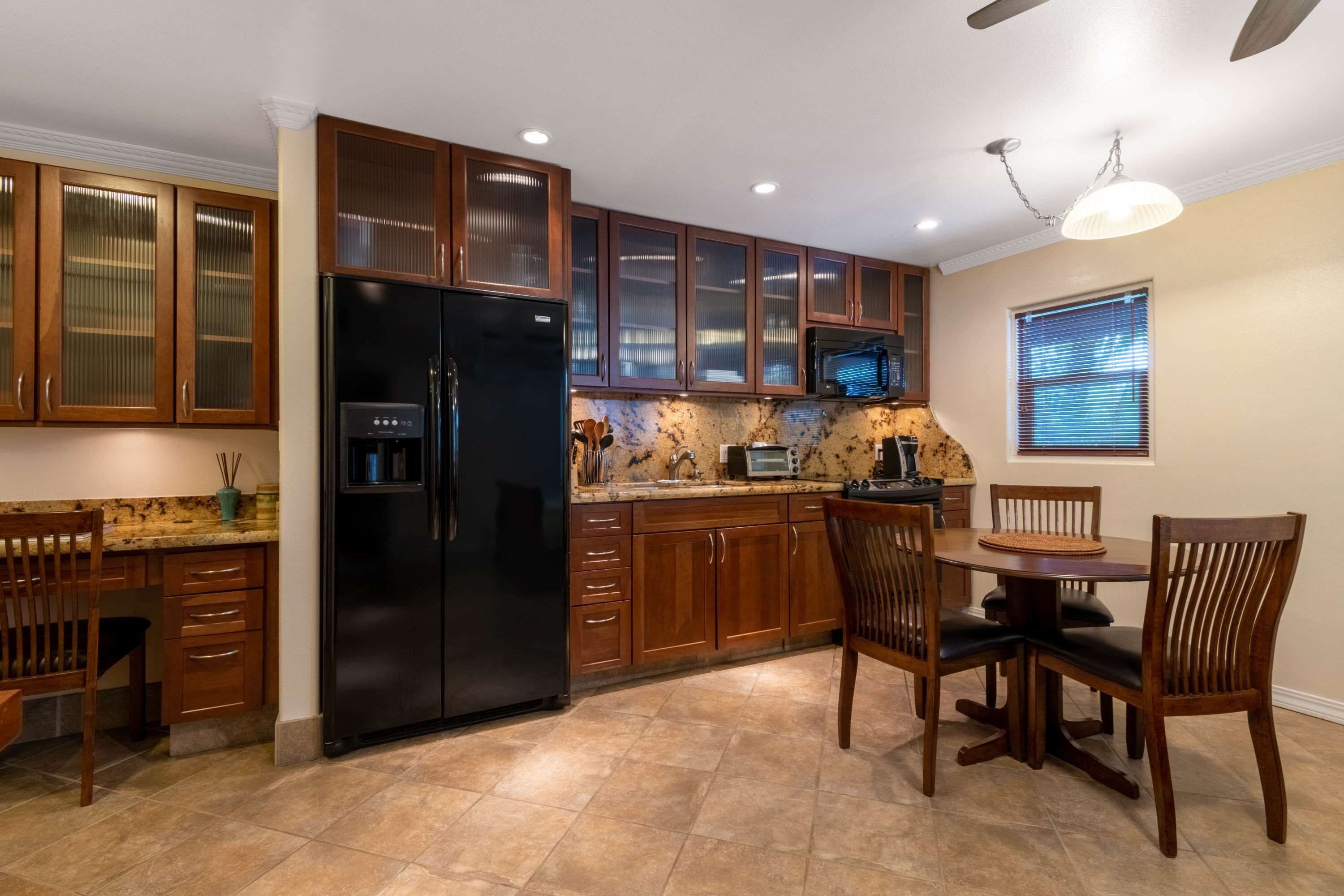 A kitchen with wooden cabinets, a black refrigerator, a dining table with chairs, and a microwave.