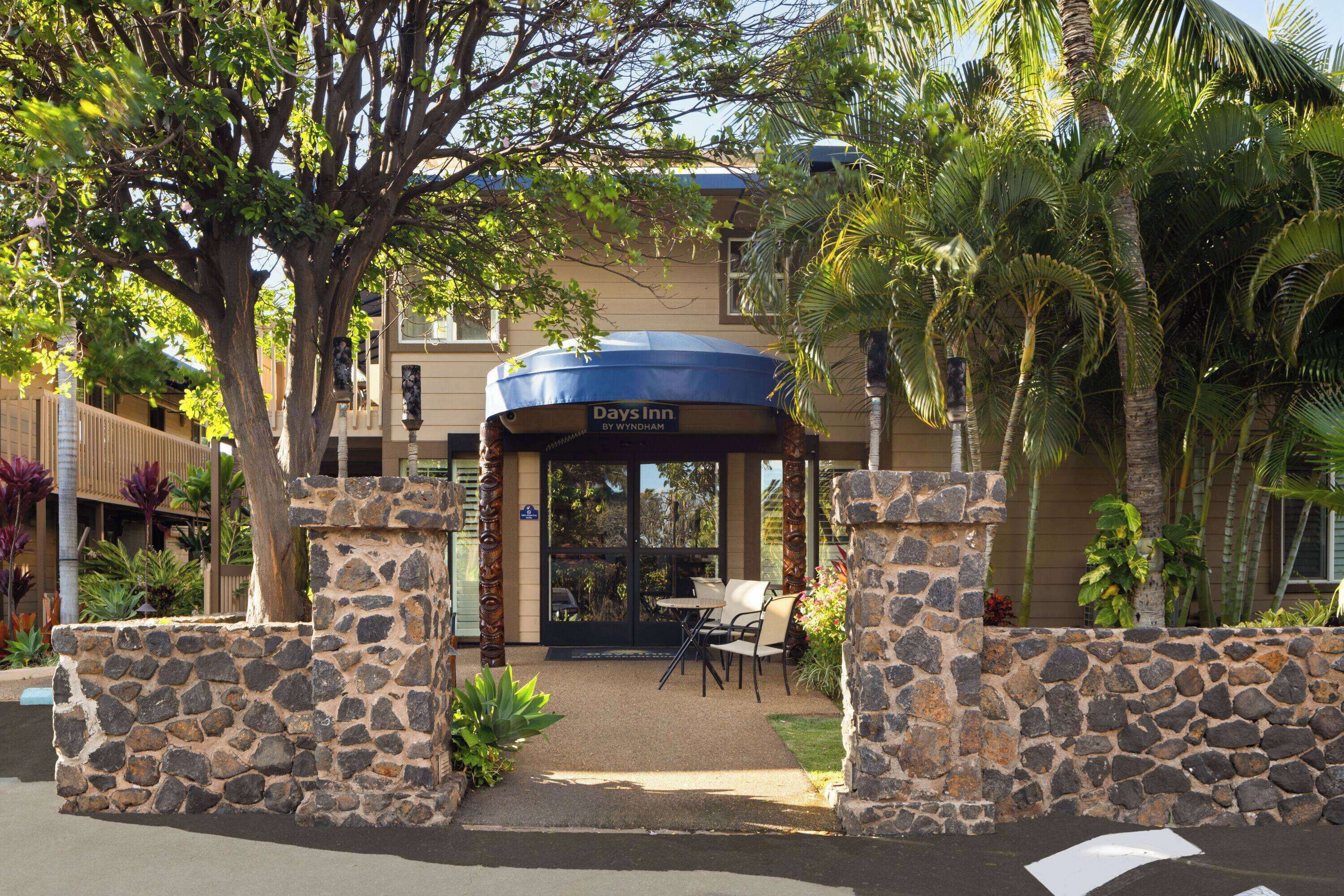 Un hotel Days Inn by Wyndham con una entrada de piedra, asientos al aire libre y palmeras.