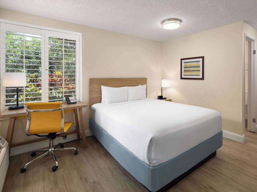Ein Hotelzimmer mit Bett, Schreibtisch, Stuhl und einem Fenster mit Jalousien.