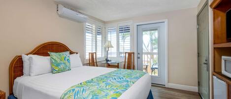 A bedroom with a large bed, a desk, and a door leading to a balcony.