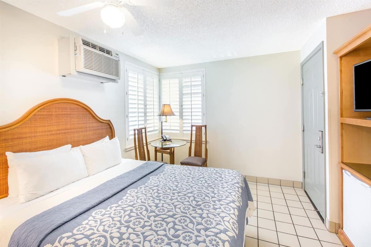 A hotel room with a bed, a desk, a chair, a television, and an air conditioning unit.