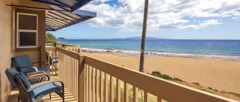 A balcony with wicker chairs and a view of the beach and ocean.