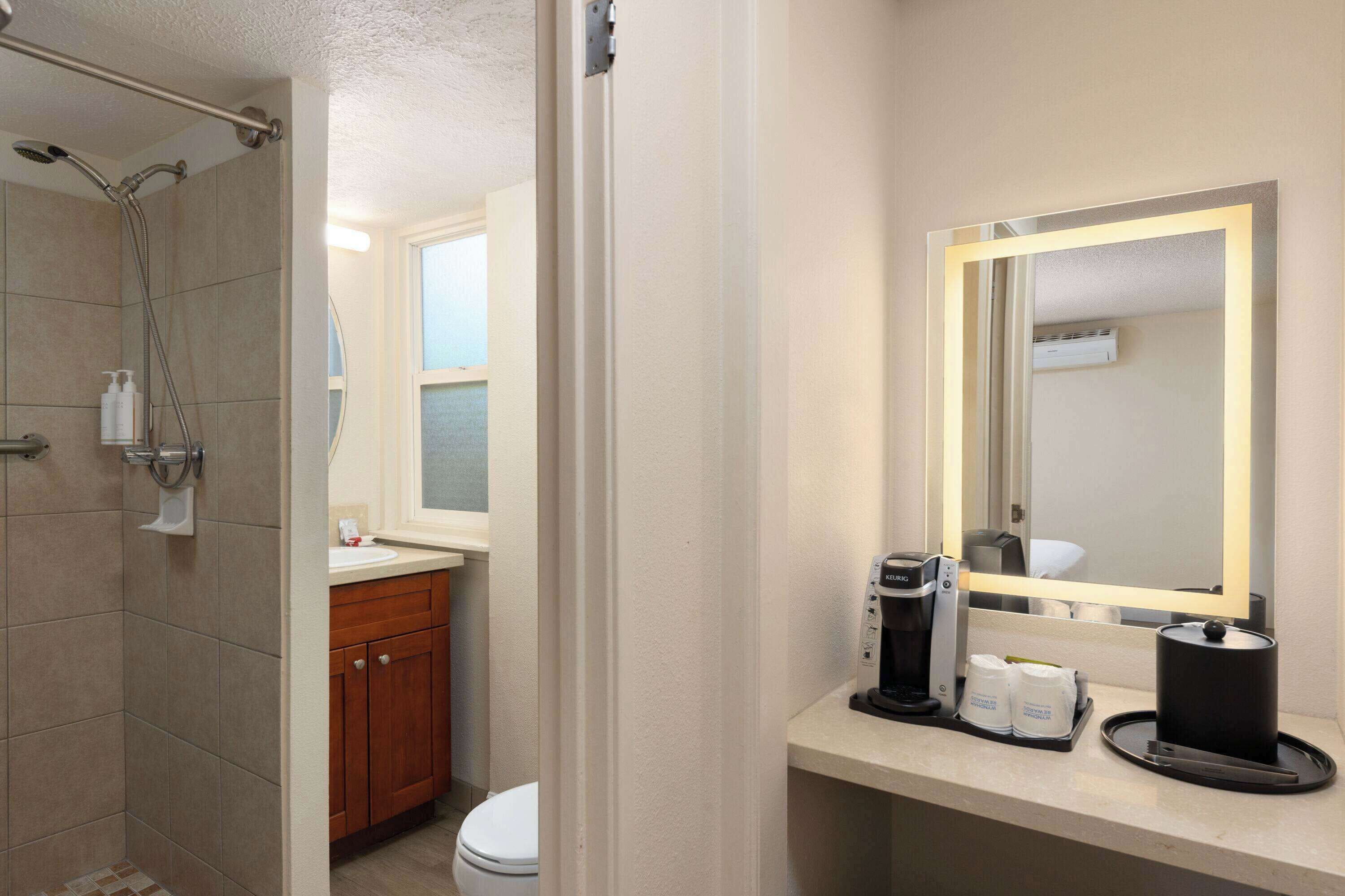 A bathroom with a shower, toilet, sink, and a mirror with a light.