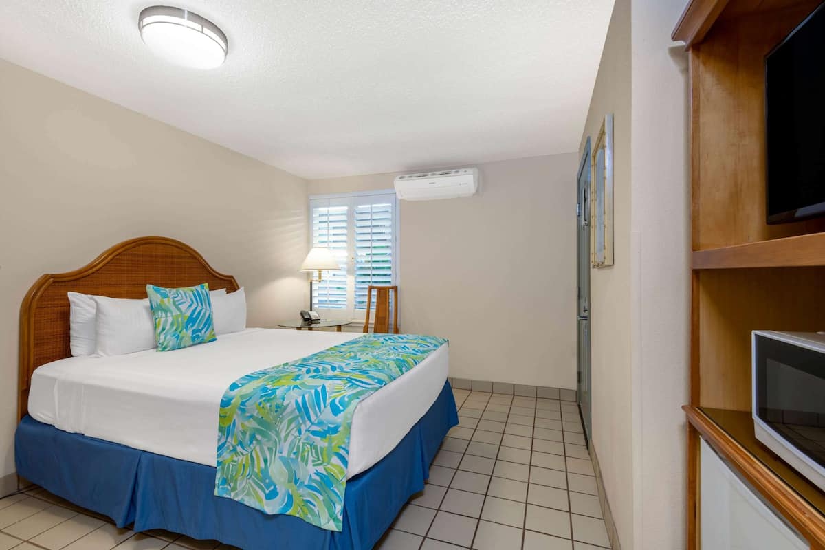 A hotel room with a bed, a TV, an air conditioning unit, and a window with blinds.