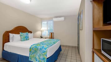 A hotel room with a bed, a TV, an air conditioning unit, and a window with blinds.
