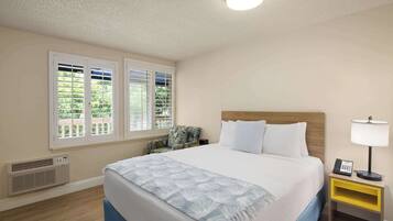 A hotel room with a bed, a nightstand, a chair, and a window with blinds.