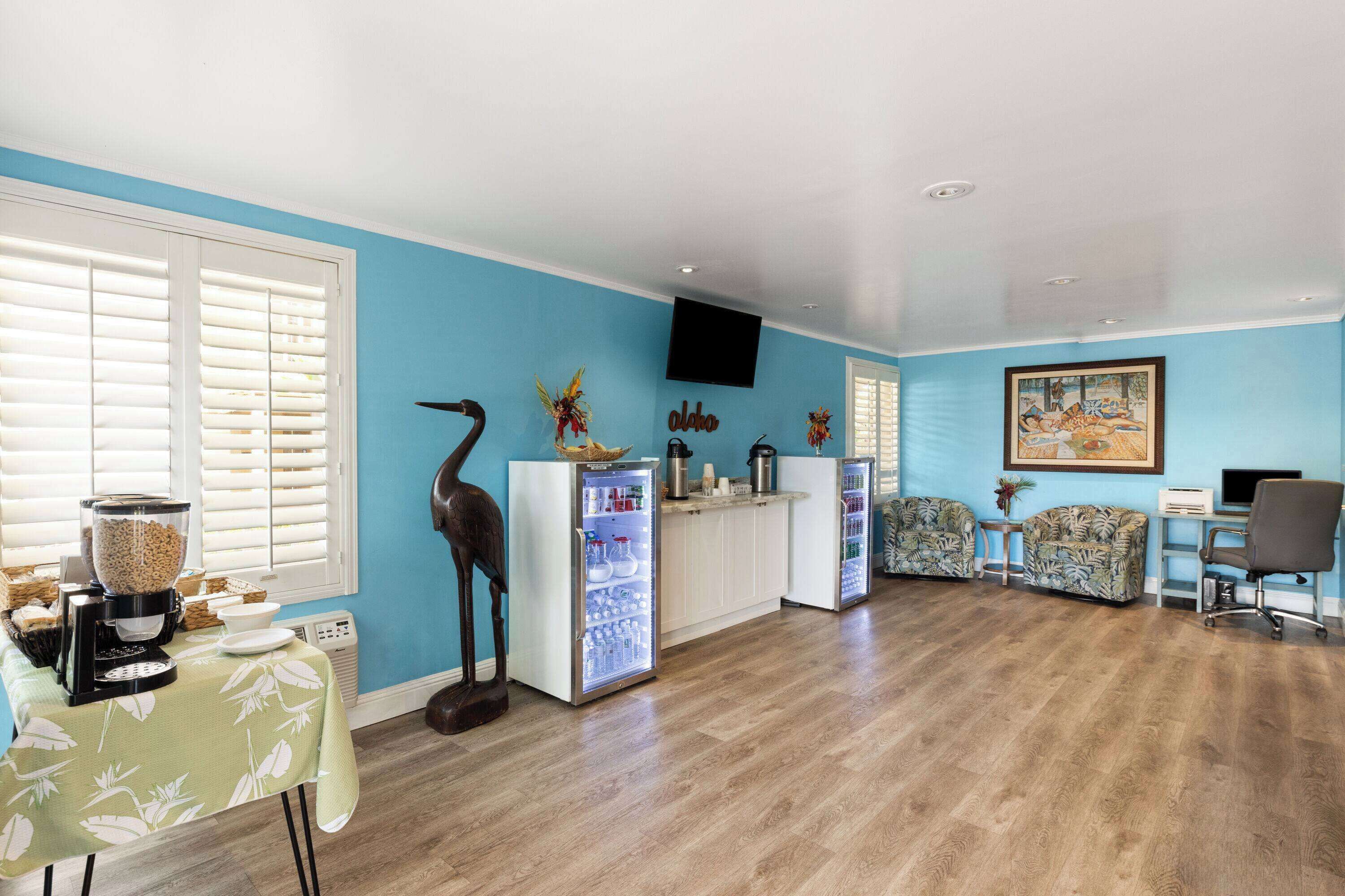 A spacious living room with a large window, a coffee station, a refrigerator, and a seating area with two sofas.
