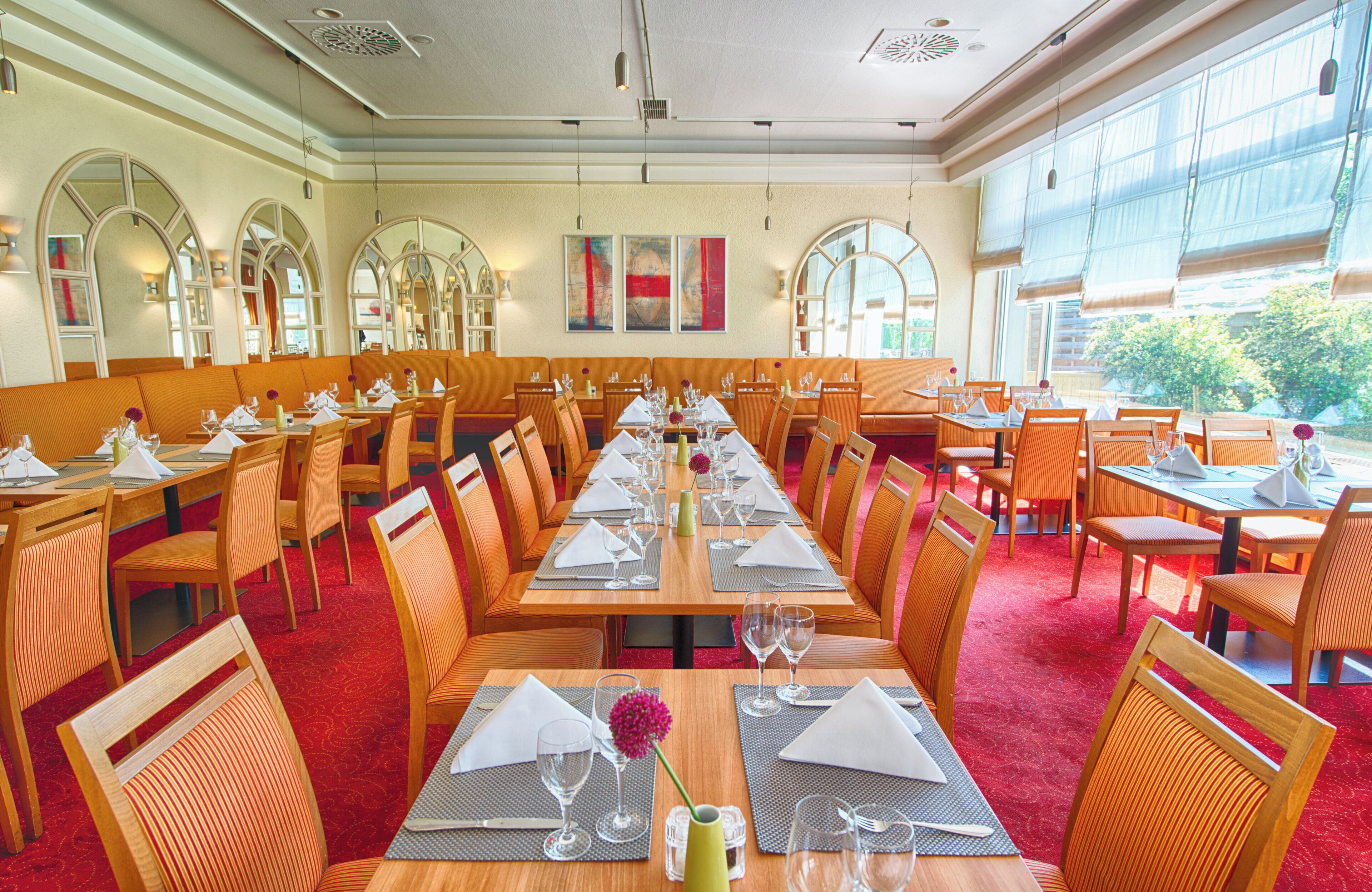 En restaurang med långa bord, orangefärgade stolar och en röd matta.