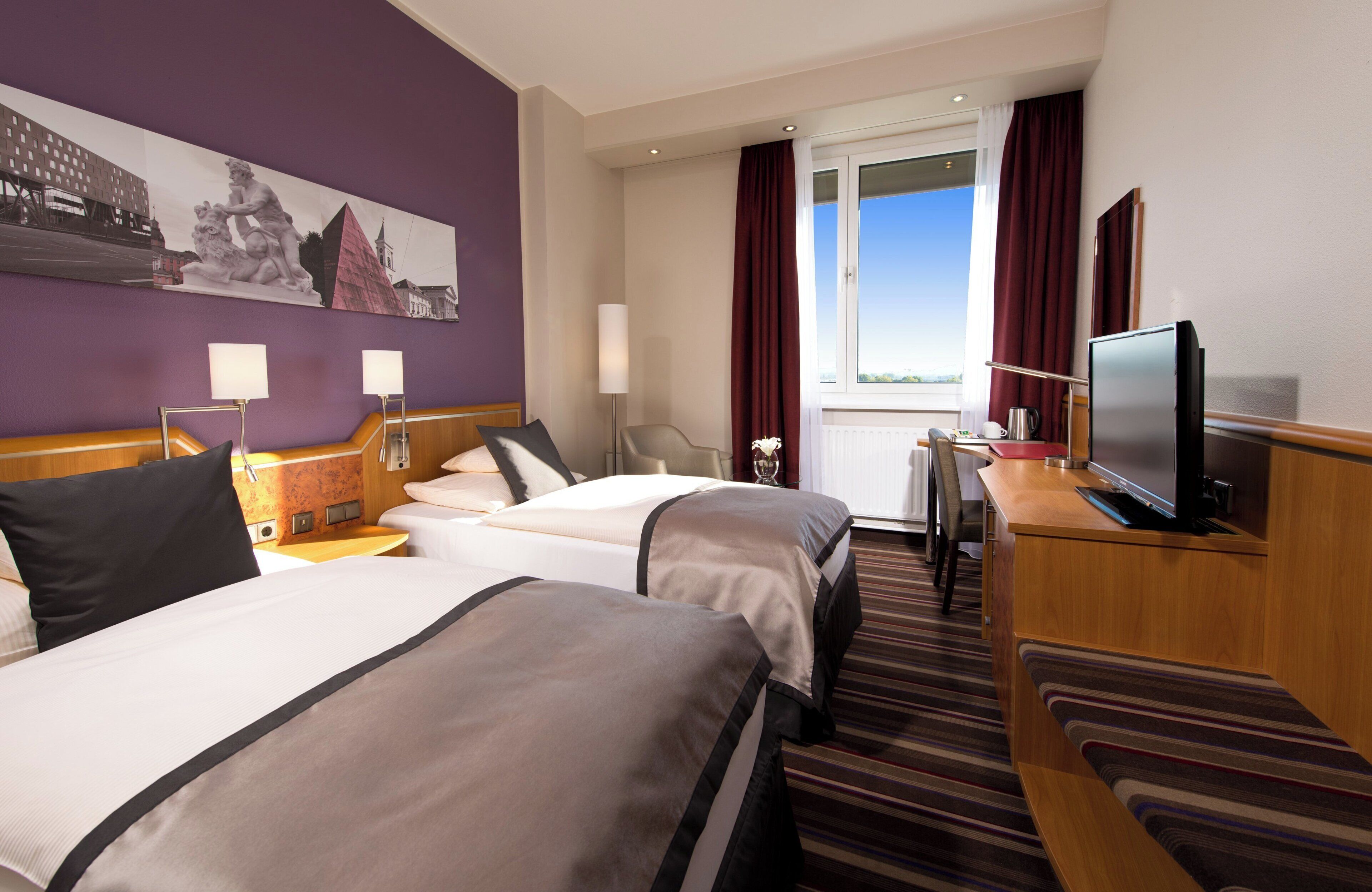 A hotel room with two beds, a television, a desk, and a view of the city.