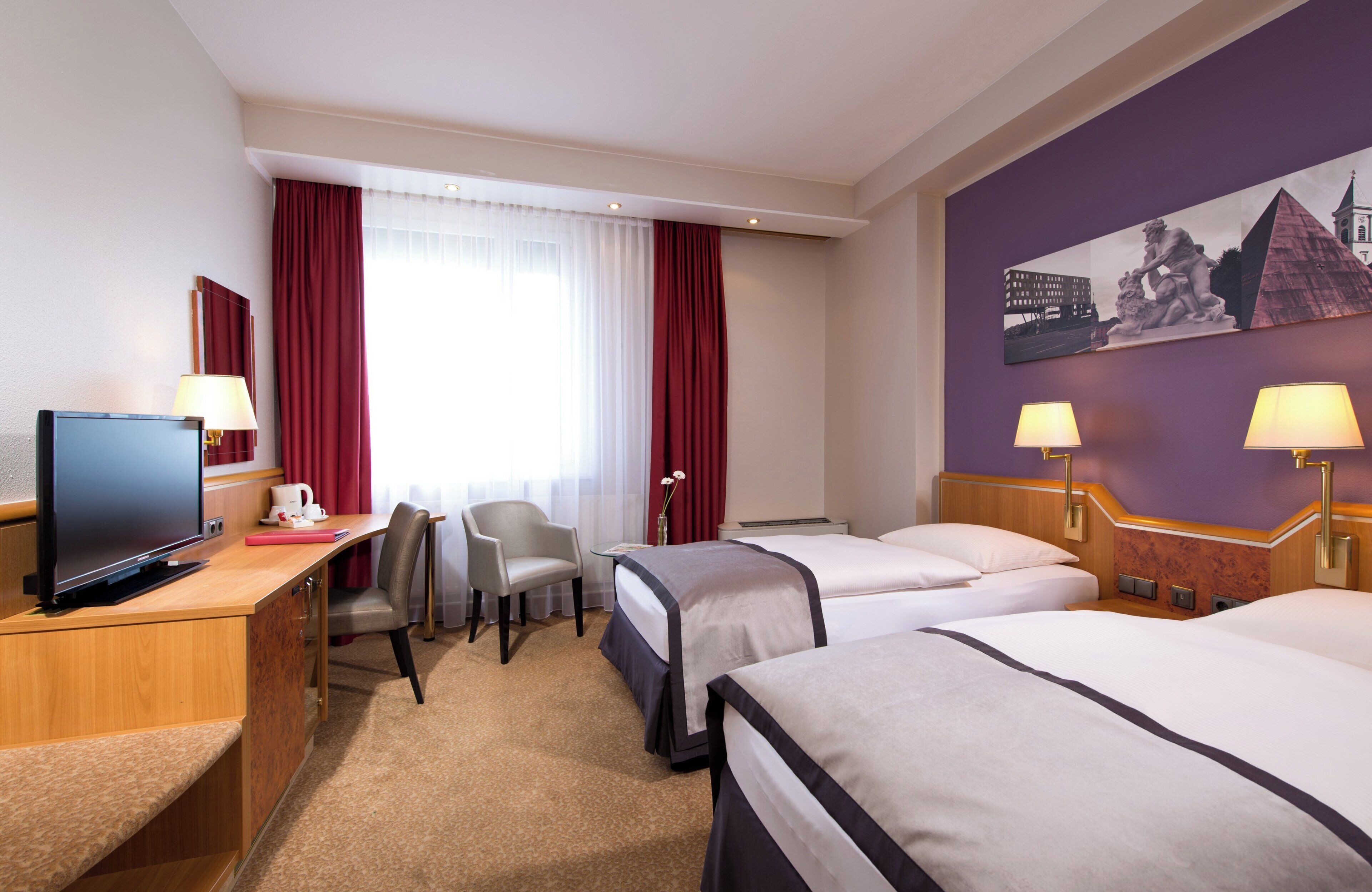A hotel room with two beds, a desk with a TV, a chair, and a large painting on the wall.