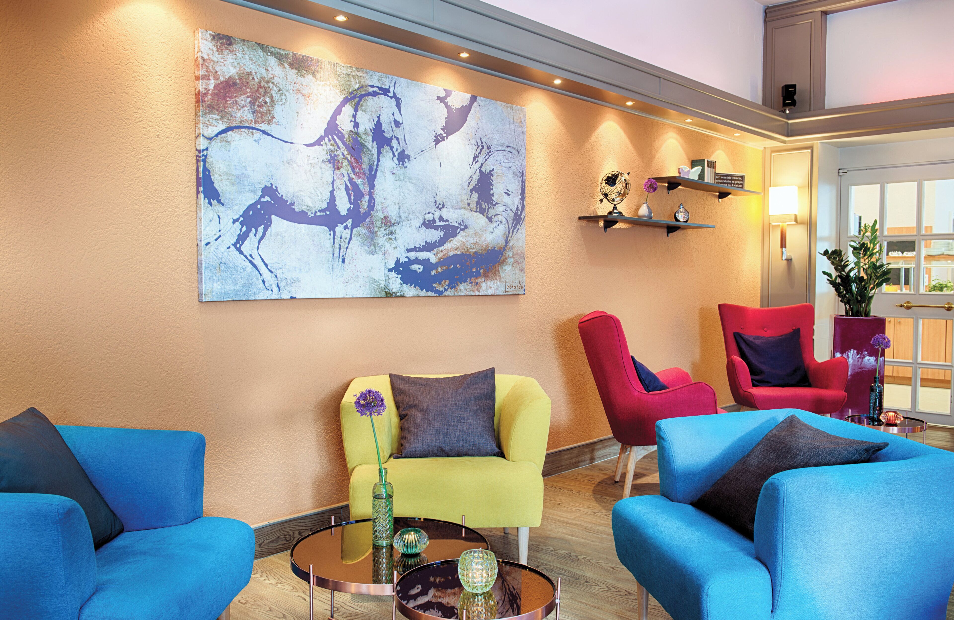 A modern lobby with a large abstract painting, bright blue sofas, and red chairs.