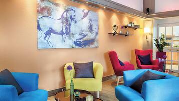 A modern lobby with a large abstract painting, bright blue sofas, and red chairs.