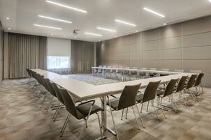 Un salón de conferencias con una larga mesa, sillas y una pantalla para proyector.