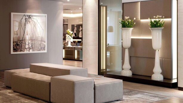 A modern lobby with a sectional sofa, a large abstract painting, and two tall vases with flowers.