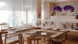 A modern restaurant with wooden tables and chairs, a reception desk, and purple flowers on display.