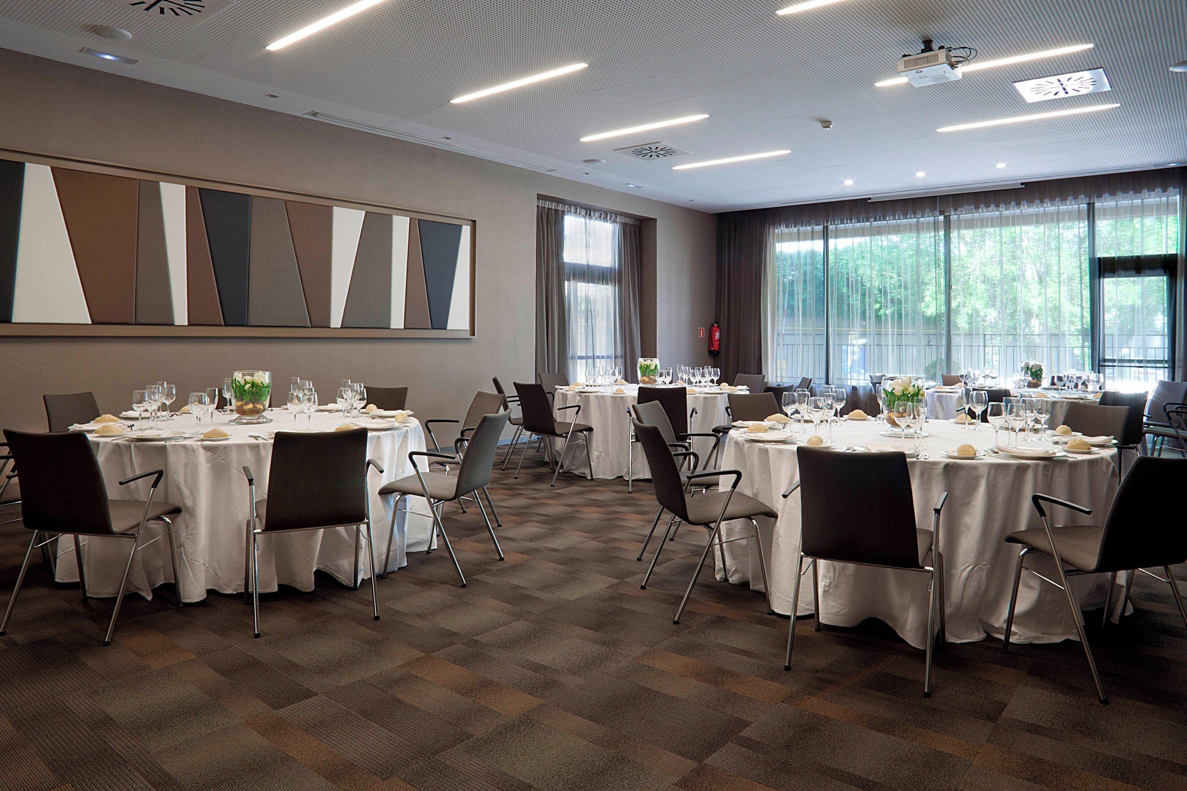 Un salón de conferencias con varias mesas redondas, cada una con sillas, manteles blancos y copas.