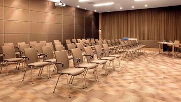 Un salón de conferencias con filas de sillas, un proyector y una mesa con botellas de agua.