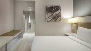 A modern hotel room with a bed, bedside table, and a wall-mounted artwork.