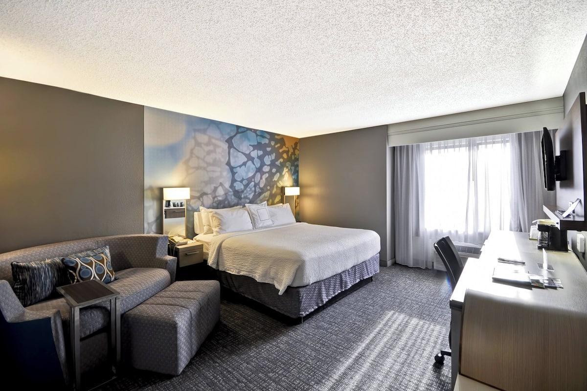 A hotel room with a bed, a sofa, a desk, and a TV.