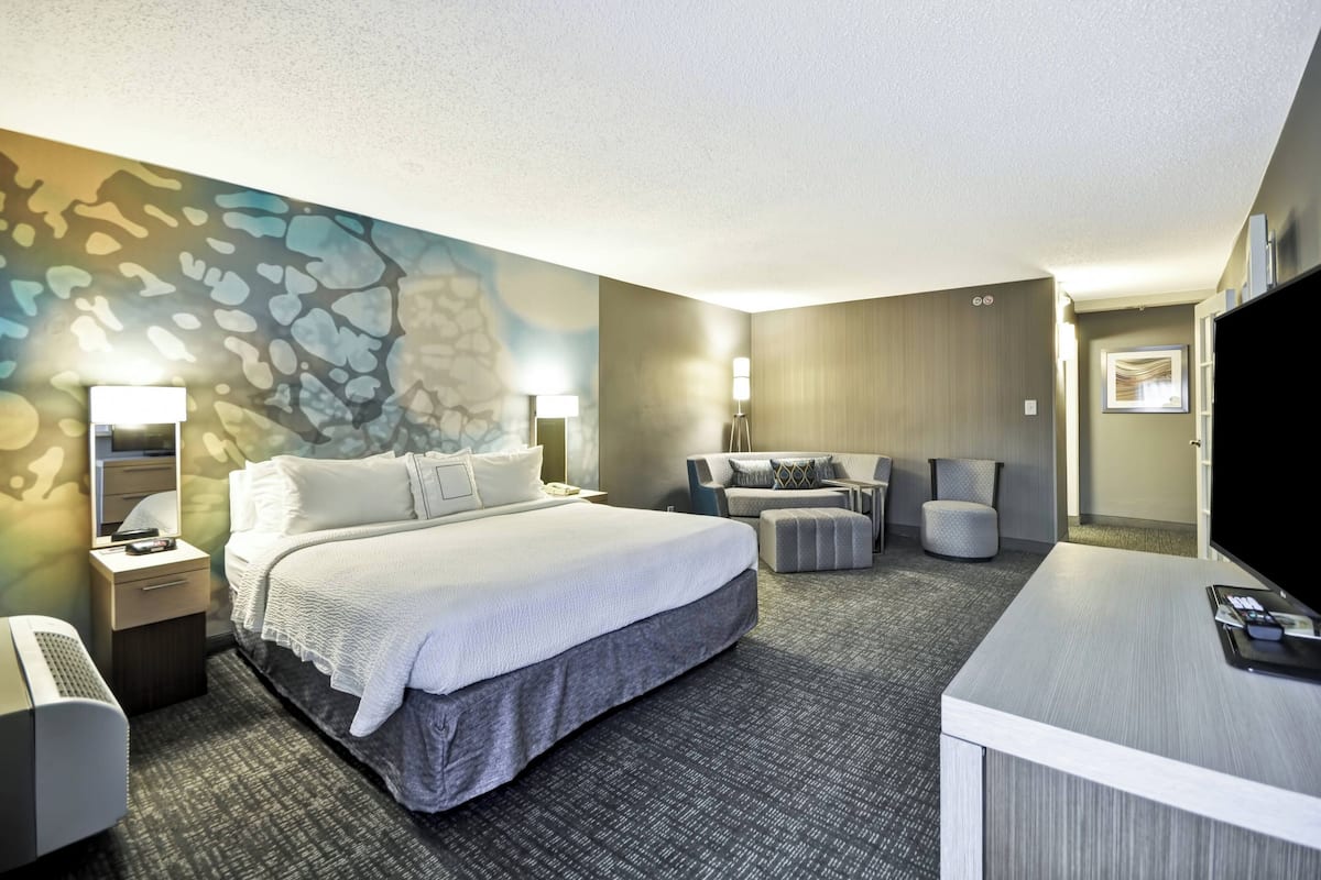 A hotel room with a large bed, a desk, a chair, and a television.