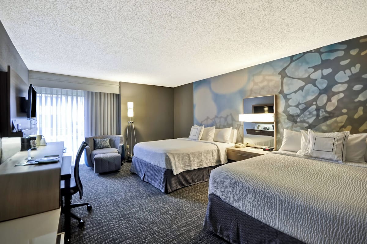 A hotel room with two beds, a desk, a chair, a TV, and a window with curtains.