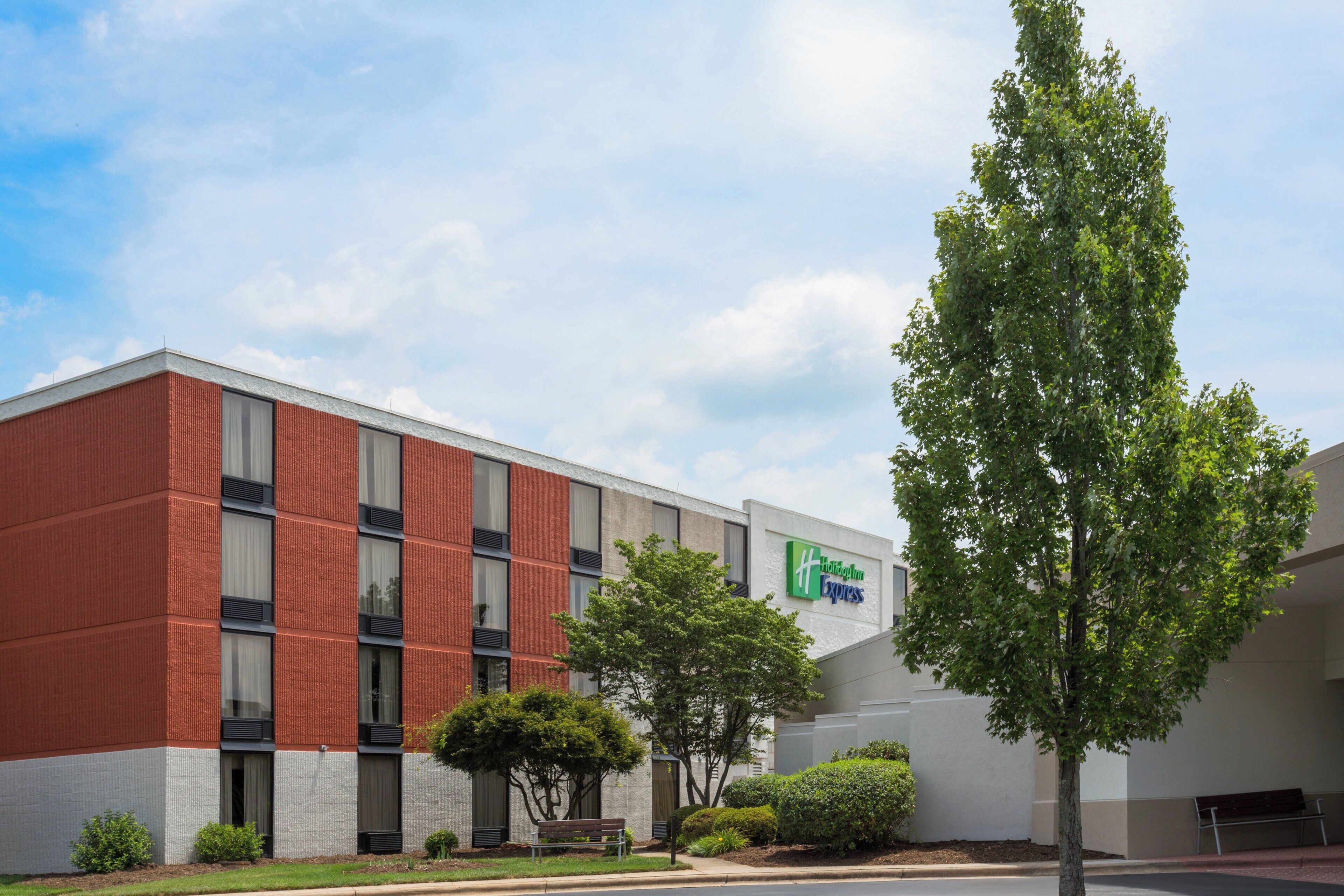 Ein modernes Gebäude mit roter Backsteinfassade, einem Holiday Inn Express Schild und einem gepflegten Rasen mit einer Bank.