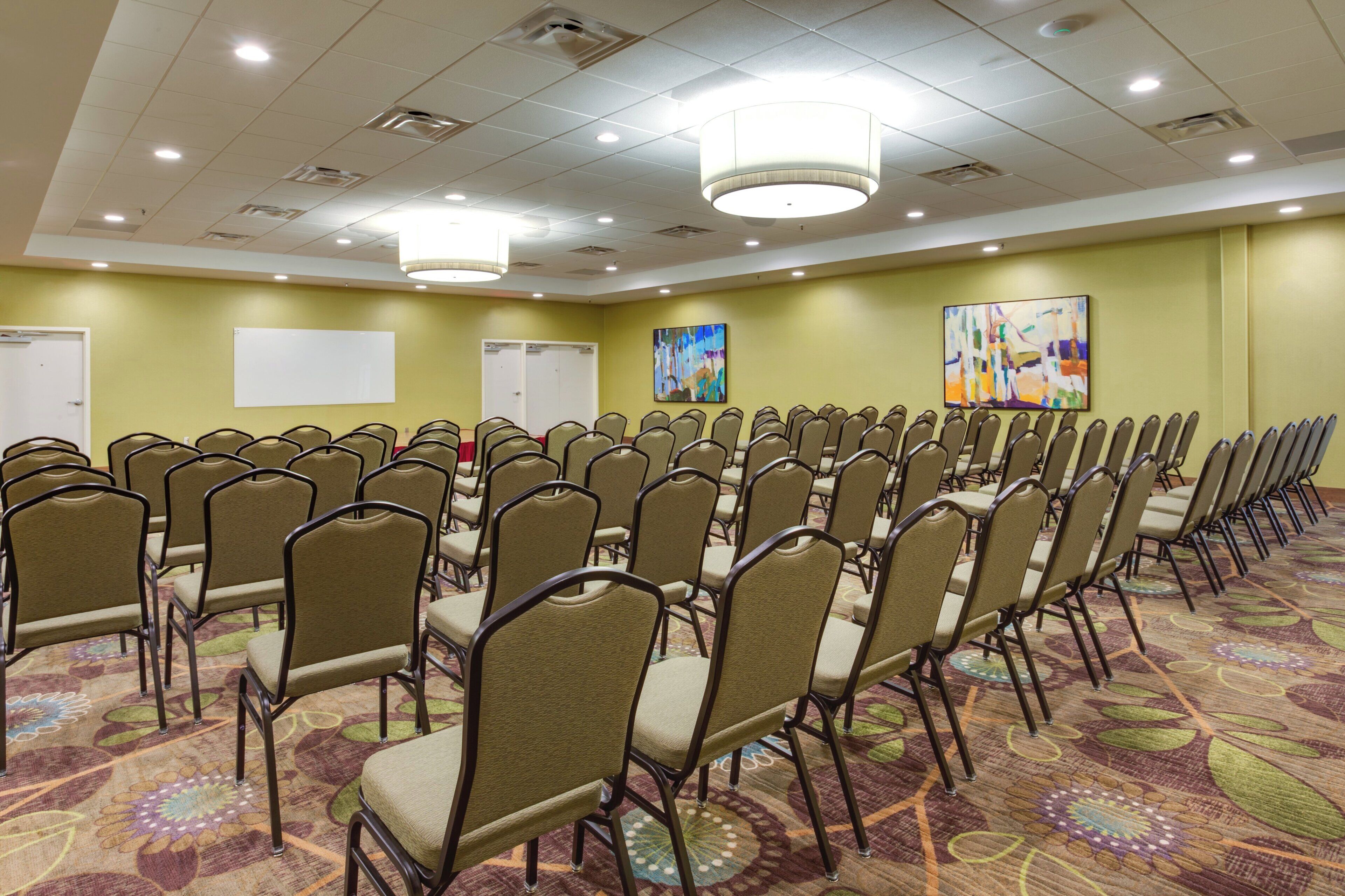 A conference room with rows of chairs, a whiteboard, and two paintings on the walls.