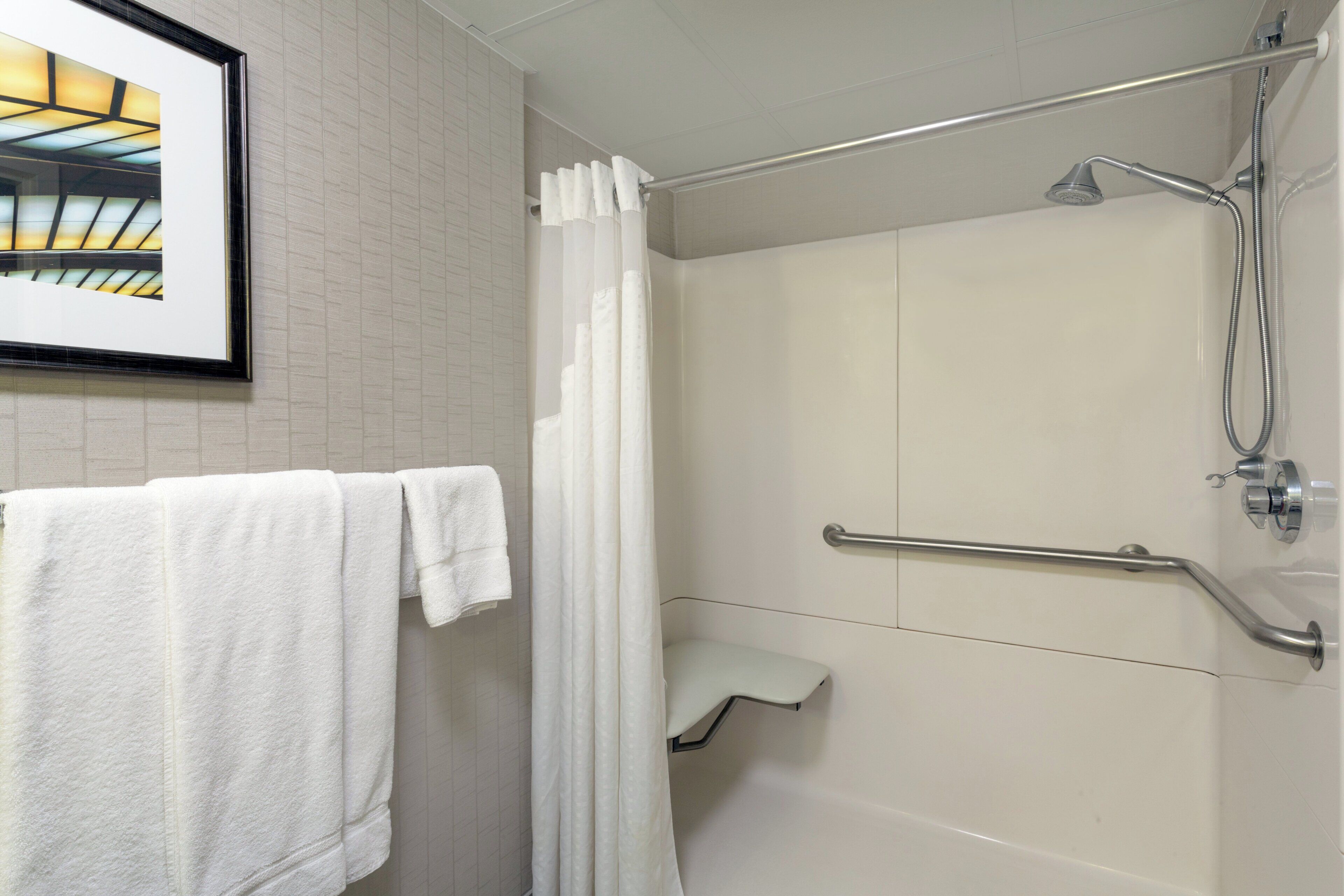A bathroom with a shower, a white towel on the wall, and a framed picture above the mirror.