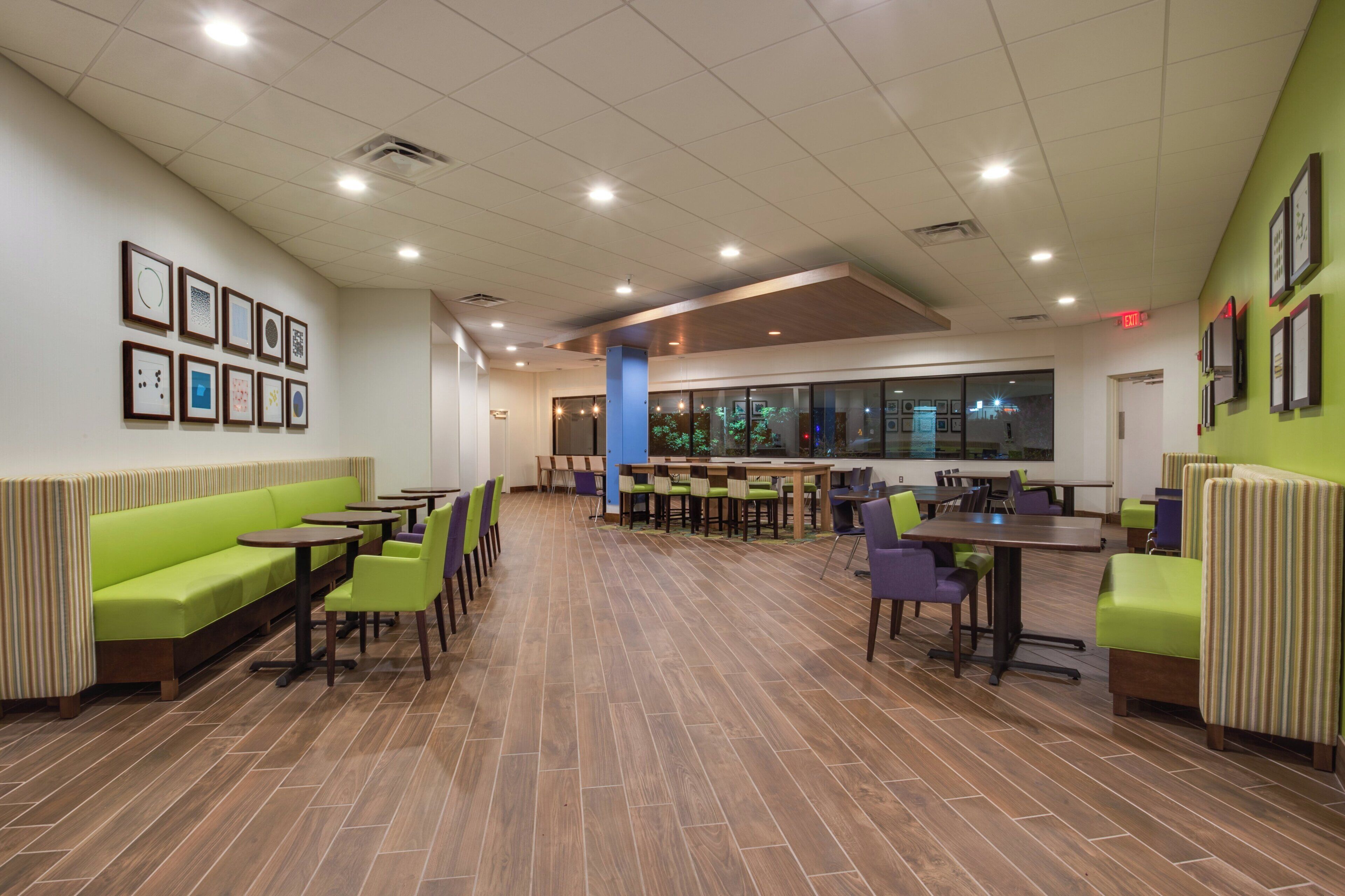 Un comedor interior amplio con mesas y sillas altas, un banco acolchado verde y cuadros en las paredes.