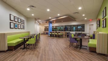 Un comedor interior amplio con mesas y sillas altas, un banco acolchado verde y cuadros en las paredes.