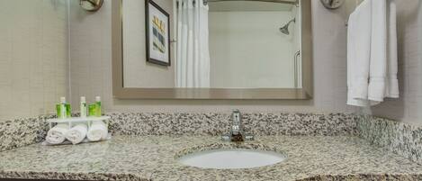 A bathroom with a granite countertop sink, a mirror, a shower, and a towel rack.
