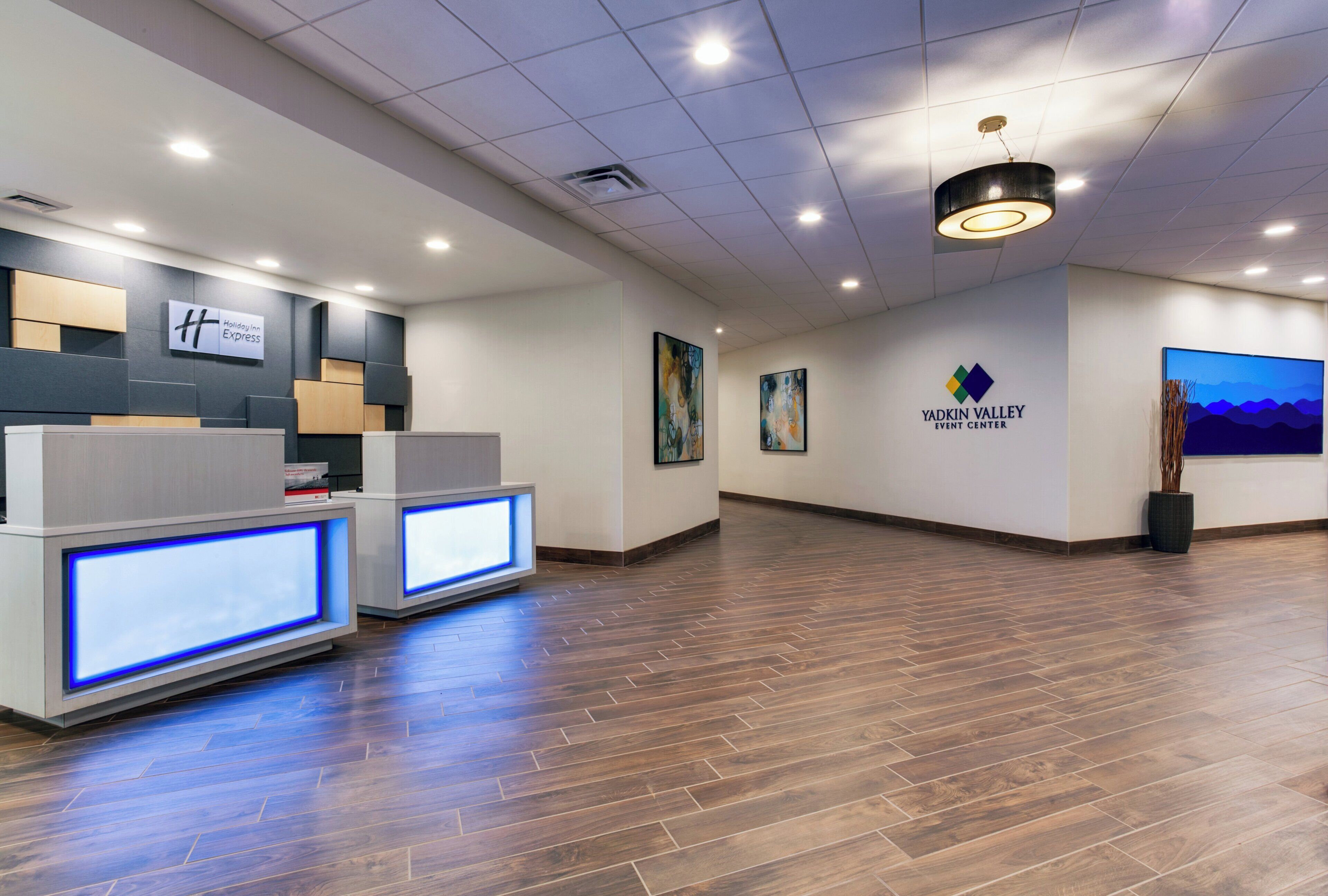 A reception area with a Holiday Inn Express sign, a Yadkin Valley Event Center logo, and a modern reception desk with illuminated panels.