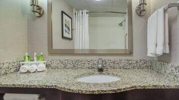 Une salle de bain avec un lavabo doté d’un plan de travail en granit, un miroir, un porte-serviettes et un tableau encadré au mur.