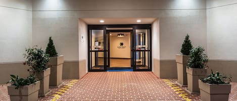 Een hotelentree met een met baksteen bestraat pad dat leidt naar dubbele deuren, met potplanten aan weerszijden, en een bord voor het Yakkin Valley Event Center.