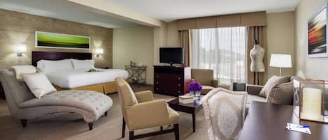 A hotel room with a bed, a desk, a chair, a sofa, a television, and a window with curtains.