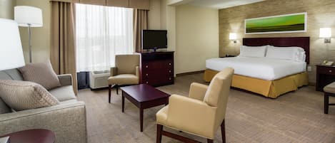 A hotel room with a bed, two armchairs, a desk, a TV, and a large window with curtains.