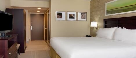 A hotel room with a large bed, a television on a wooden dresser, and three framed pictures on the wall.
