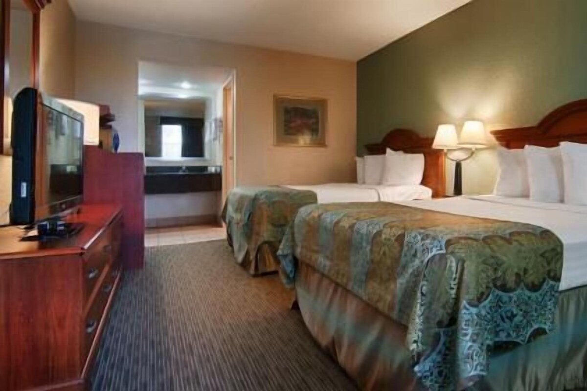 Een hotelkamer met twee bedden, een televisie, een bureau en een badkamer op de achtergrond.