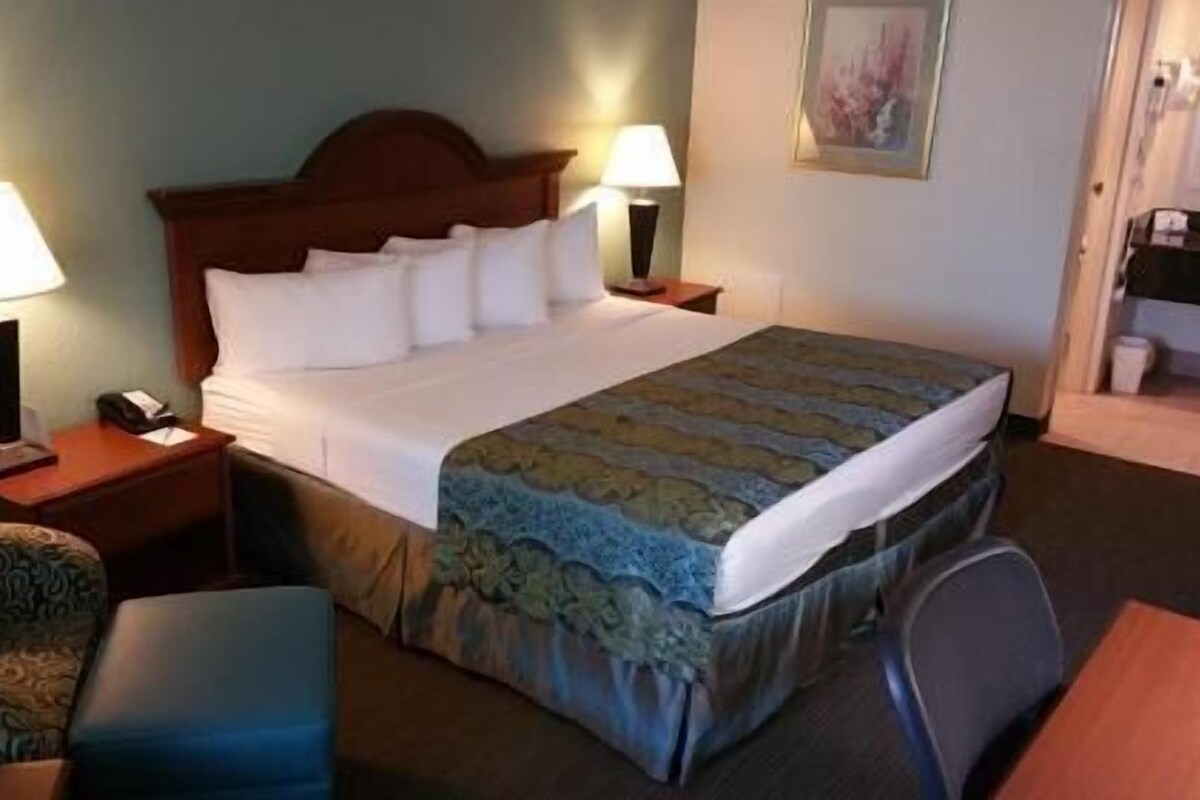 Een hotelkamer met een bed, twee bedlampen, een stoel, een bureau en een schilderij aan de muur.