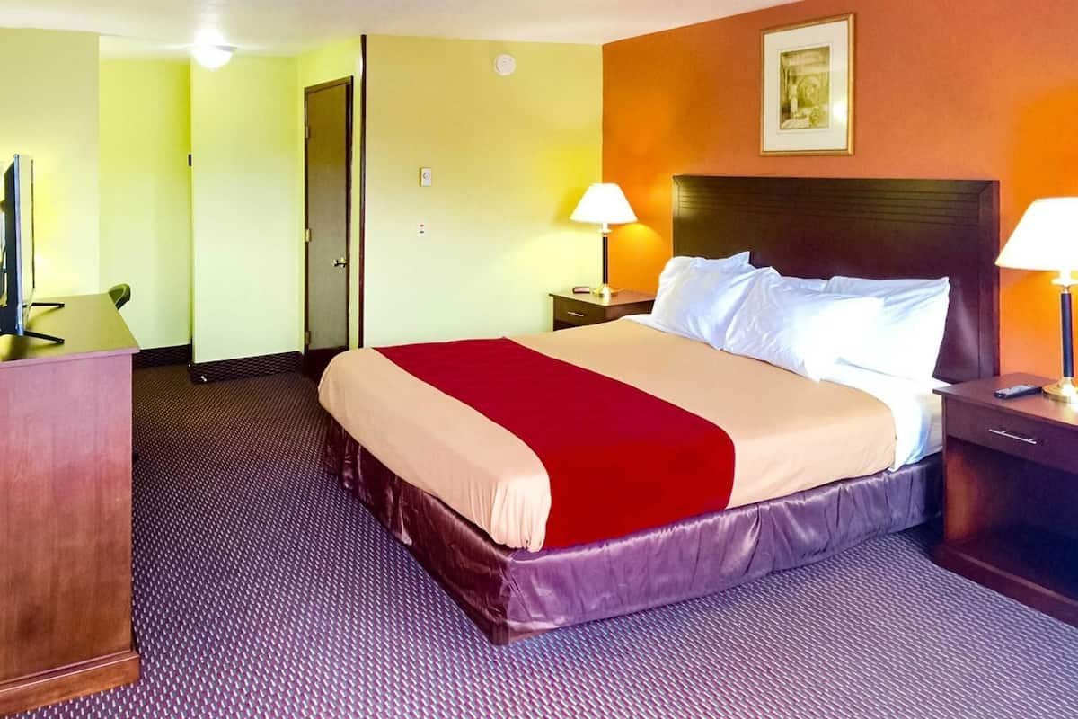 Quarto de hotel com cama, mesas de cabeceira, escrivaninha e porta.