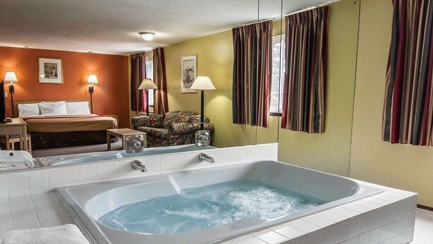 Habitación de hotel con una bañera grande, una cama, una silla y un escritorio con lámpara.