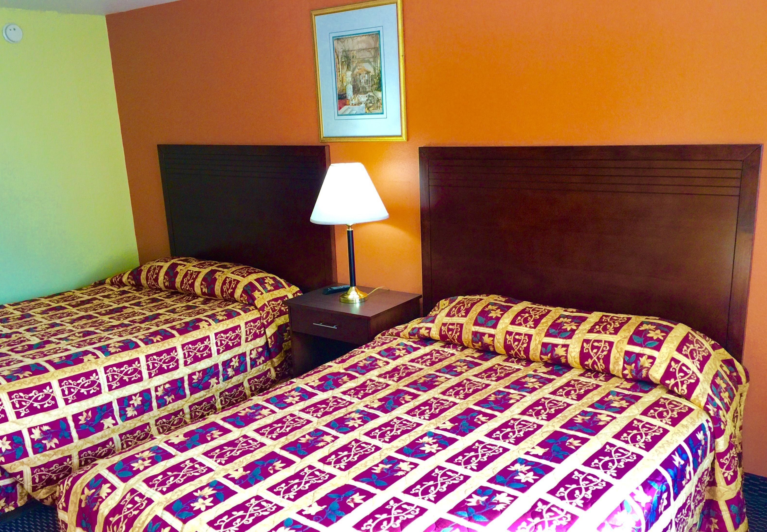 A hotel room with two beds, each with patterned bedding, a nightstand with a lamp, and a framed picture on the wall.