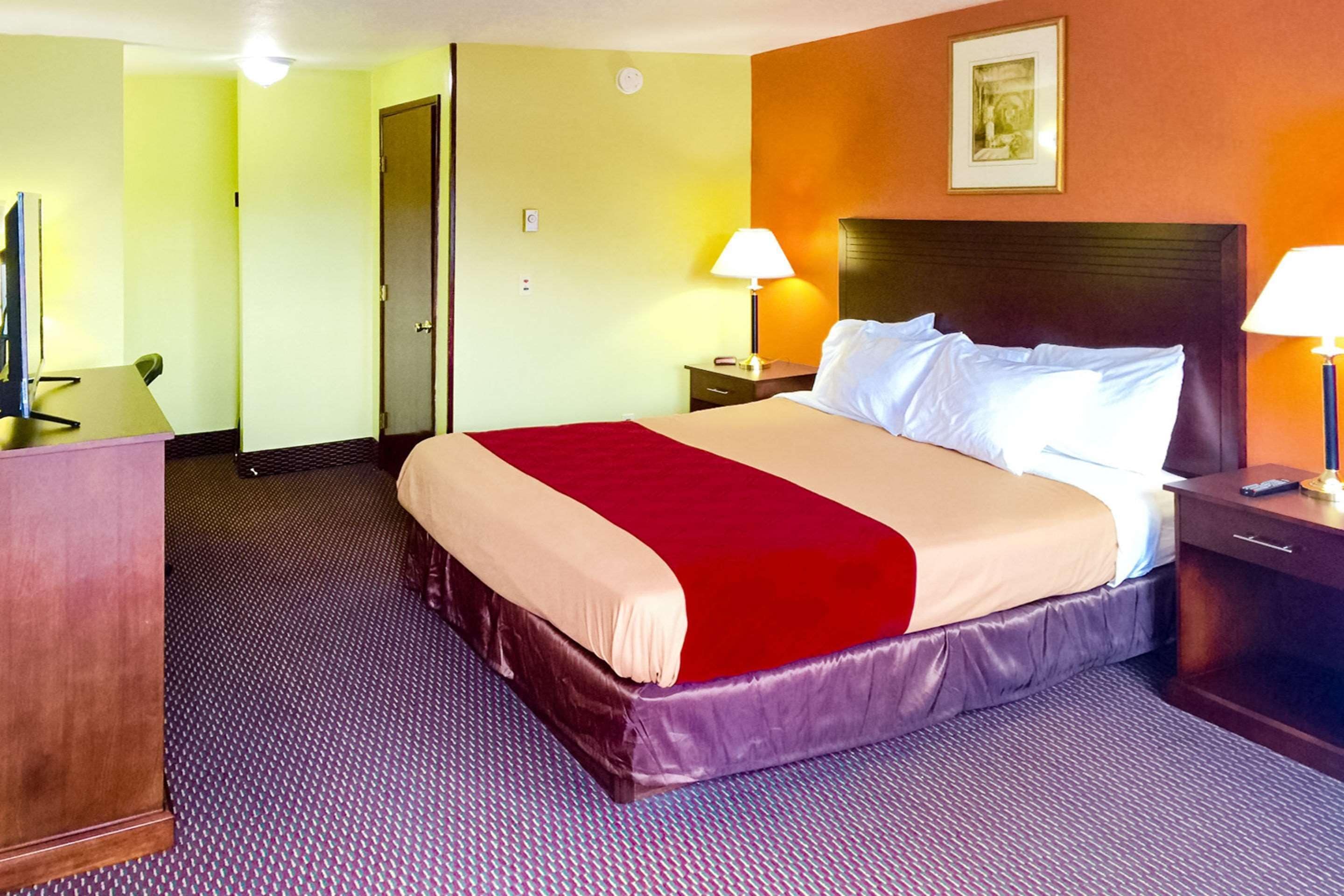 A hotel room with a large bed, two bedside lamps, a desk with a chair, and a television.