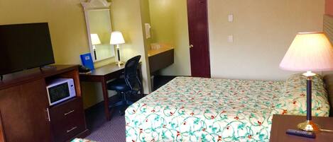 Una habitación de hotel con cama, escritorio, silla, televisión y lámpara.