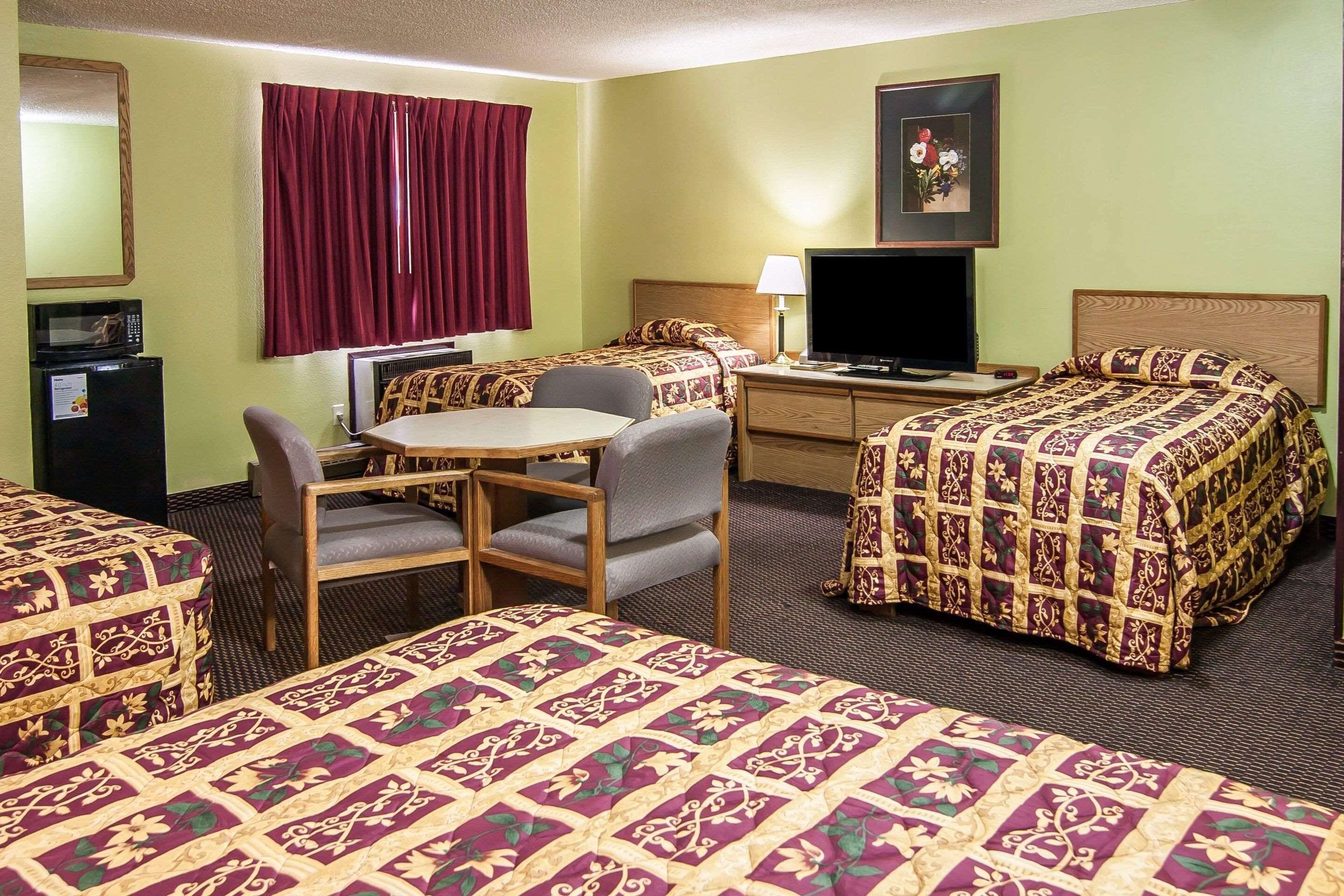 A hotel room with two beds, a desk with a chair, a television, and a small refrigerator.