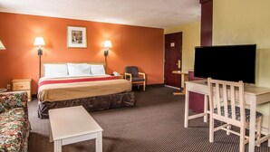 Una habitación de hotel con cama, escritorio, silla, televisor y lámpara.