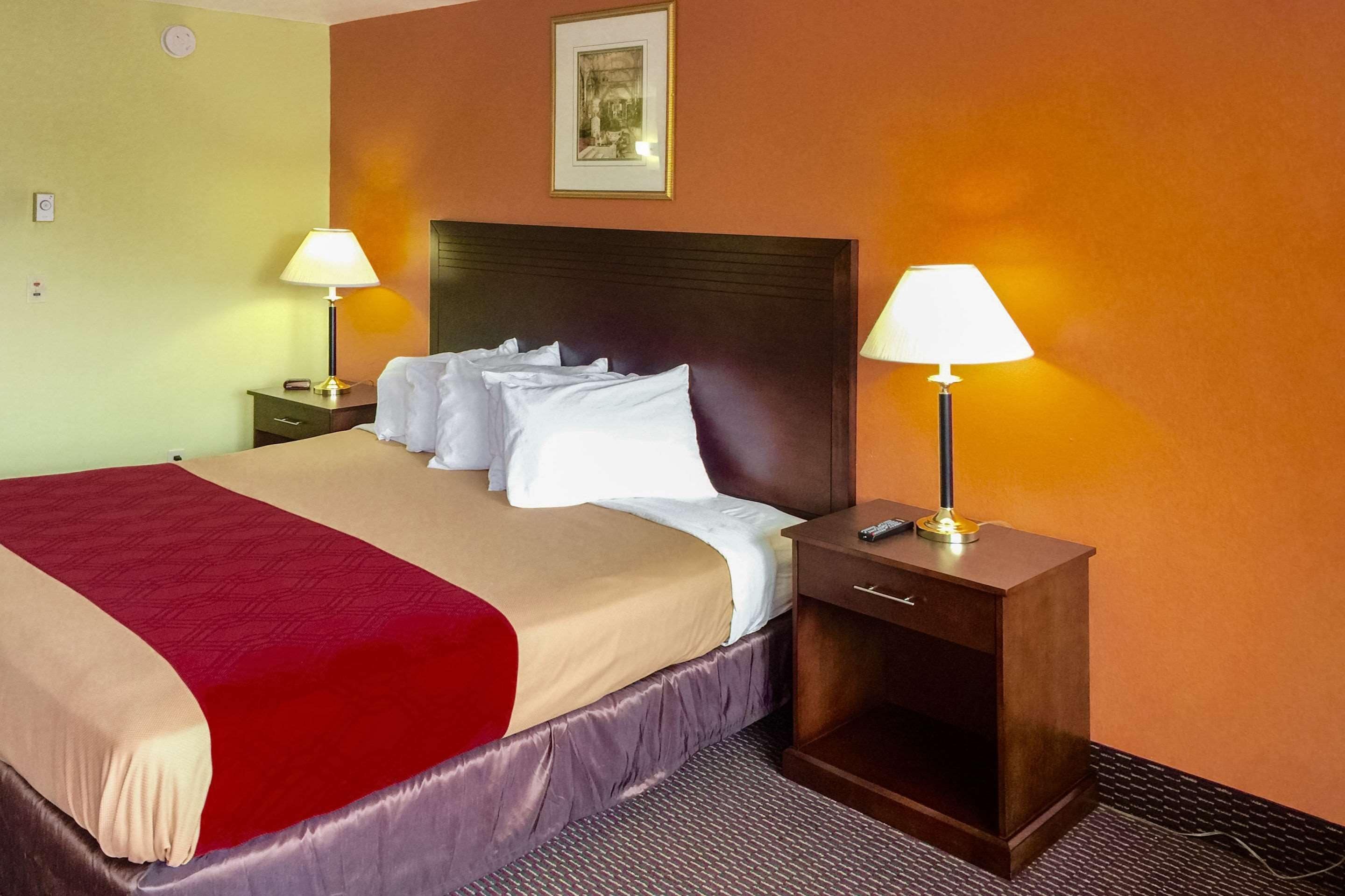 Une chambre d’hôtel avec un grand lit, deux tables de chevet avec des lampes, une horloge et un tableau encadré au mur.
